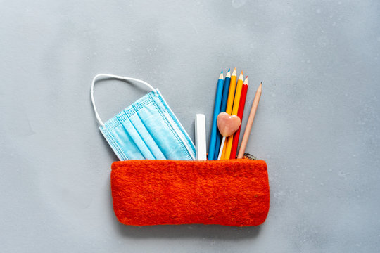 Oranges Federpenal mit Buntstiften, rosa Lutscher und Kreide auf einem grauen Hintergrund. Flat lay, Schulbeginn, neue Normalit&auml;t.