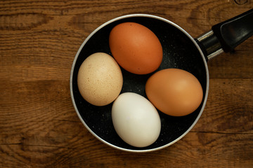 Homemade fresh colorful eggs on a frying pan and wooden background. Food background, top view.