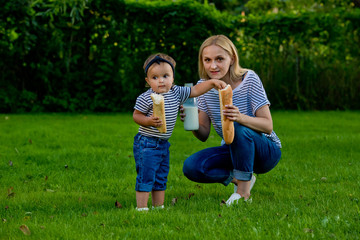 Fototapeta premium A young woman in jeans and a striped T-shirt gives her daughter fresh baguette. Family picnic.