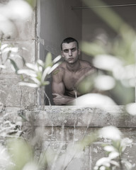 Young, muscular man staring out of a window in an abandoned building
