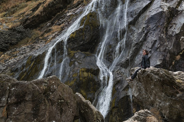 Girl sitting on a rock near waterfall.