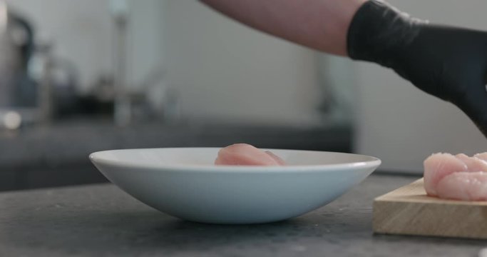 Slow motion man in black gloves put chicken fillet slices in white bowl for marinating