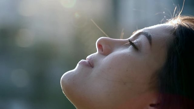 Contemplative young woman looking up to sky with faith and hope. Faithful girl profile face with lens-flare outside