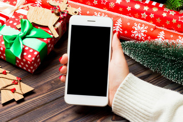 Top view of a woman holding a phone in her hand on wooden New Year background made of fir tree and...