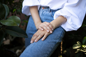 Young well-groomed hands with natural manicure of a girl in a white blouse and blue jeans. 
Beautiful female hands.