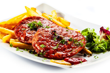Grilled steaks, French fries and vegetables on white background
