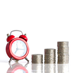 Close-up of a red clock and a pile of coins on a white background. Business Finance and Money concept. Save money to prepare for the future.