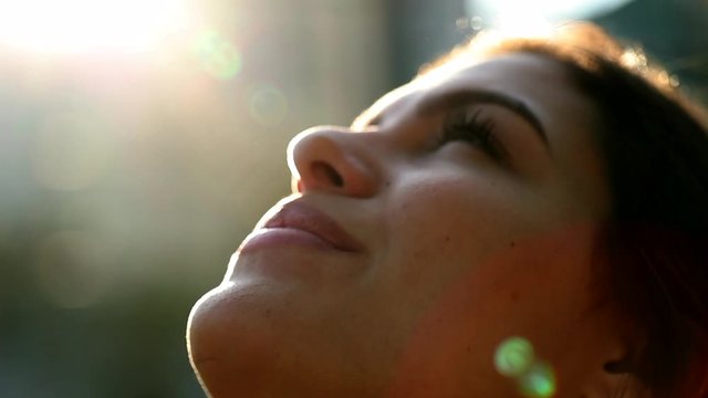 Contemplative young woman looking up to sky with faith and hope. Faithful girl profile face with lens-flare outside