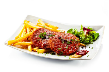 Grilled steaks, French fries and vegetables on white background
