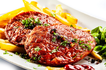 Grilled steaks, French fries and vegetables on white background
