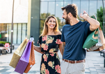 The couple is carrying bags with things they bought at the shopping mall and walking