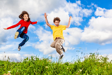 Girl and boy running, jumping against blue sky
