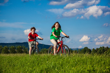 Healthy lifestyle - girl and boy riding bicycle against blue sky
