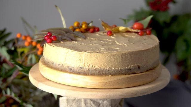 Brown mousse cake decorated with autumn leaves and berries is rotating on a wooden stand. Concept of autumn atmosphere and mood