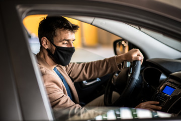 Fototapeta na wymiar A man drives a car with a mask on his face and adjusts the music in the car, life during a pandemic caused by a virus
