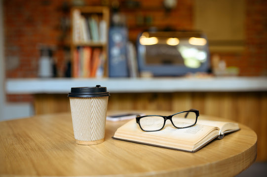 Book, coffee and glasses on table in student cafe