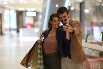 A couple satisfied with shopping is standing in the shopping mall and taking photos of them, they smile