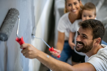 Father and mother with a smile on their face paints the wall while the son watches, the family paints their new apartment together