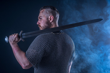 Studio photography: half-length portrait of a Viking in chain mail and holding a sword in smoke
 - obrazy, fototapety, plakaty