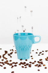 Coffee beans falling into blue cup on white background