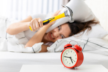 Young woman with a hammer trying to hit an alarm clock.