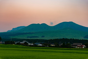 Fototapeta na wymiar 夏の空の夕日のグラデーションを背景に阿蘇山とふもとの緑の全景が雄大で美しい風景を見せる。
