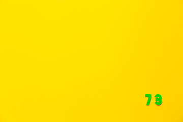 A green plastic toy number seventy-three is located in the lower right corner on a yellow background