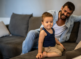 Father and son sit in the living room and spend time together, father smiles and look at his child