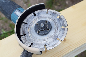 Angle grinder with disk for cutting metal on wooden plank outdoors, close up view.

