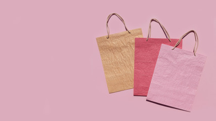 Colourful textured paper shopping bags on pink background. Minimal fashion shopping online concept. Copy space, top view, flat lay.