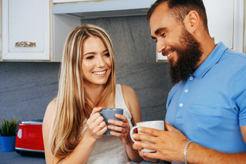 Young woman and man relaxing with cups of tea at home in kitchen