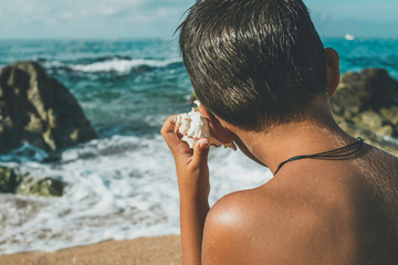 
Child listens to the sound of the sea with a conch shell in front of the beach
Conceptual of...