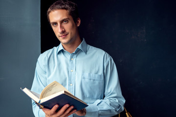 young man reading a book, a guy in a blue shirt on a dark blue background.