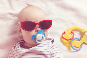 The baby lies in sunglasses and with a pacifier in his mouth