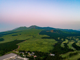 夏の空の夕日のグラデーションを背景に阿蘇山とふもとの緑の全景が雄大で美しい風景を見せる。