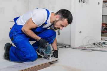 A carpenter in overalls cuts planks and lays laminate flooring
