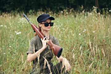 Woman on nature Sits in a shelter with a weapon dark glasses black cap green 