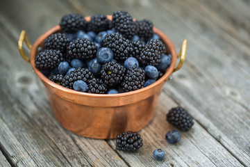 Ripe blackberries and blueberries in a vintage copper bowl. Selective focus.