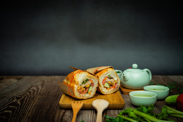 Fototapeta na wymiar Famous Vietnamese food is Banh mi thit and hot tea, popular street food from bread stuffed with raw material: pork, ham, pate, egg and fresh herbs.Typical Vietnamese sandwich
