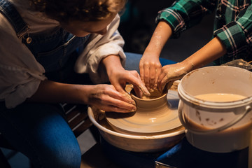 a young mother with a charming son in a pottery workshop sculpting a vase.