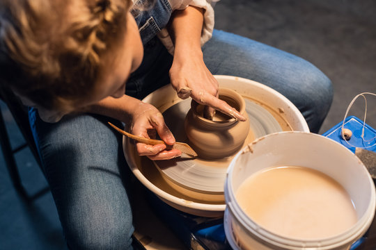 a young Potter girl in her Studio sculpts a pot with her hands and tools.
