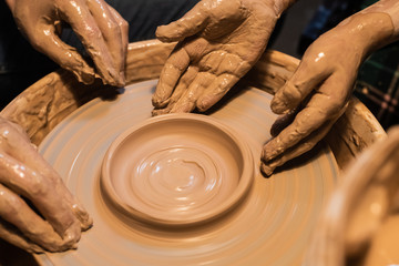teacher and student sculpt a pot of clay on a Potter's wheel, close-up.
