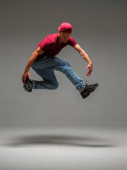 Fototapeta na wymiar Cool young guy breakdancer jumps in studio on gray background. Battle competitions announcement