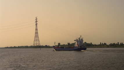 Fototapeta premium Elbe river near Hamburg harbor with huge power line and a ferry sailing by to deliver green energy from wind turbines during warm sunset, Germany
