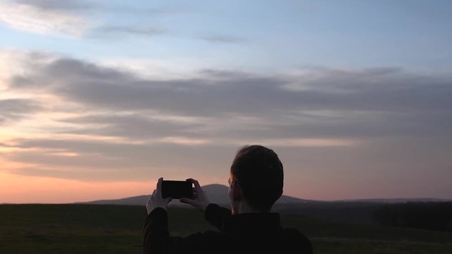 Man hands holding mobile phone and taking, shoot picture, video at sunset.guy taking photo of sunset with telephone, smartphone at sunrise.