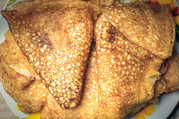 Juicy pancakes cooked in pan lie in small saucer on kitchen table.