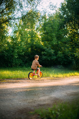 Cute little boy rides a bicycle on a path in nature. Learning to ride a bicycle. Summer walks