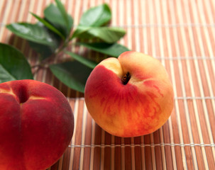 Closeup fresh Peaches fruit with green leaves on bamboo placemat background.