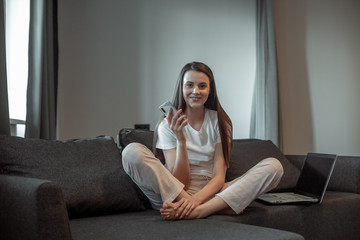 Young woman with modern laptop sitting on sofa at home