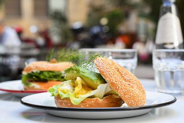 Delicious avocado egg bagel on white plate on a table in a cafe. top view